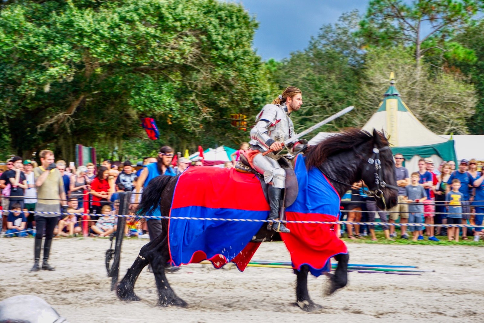 A knight on horseback wielding a sword charges toward a young man unwittingly holding an apple at the Sarasota Medieval Fair