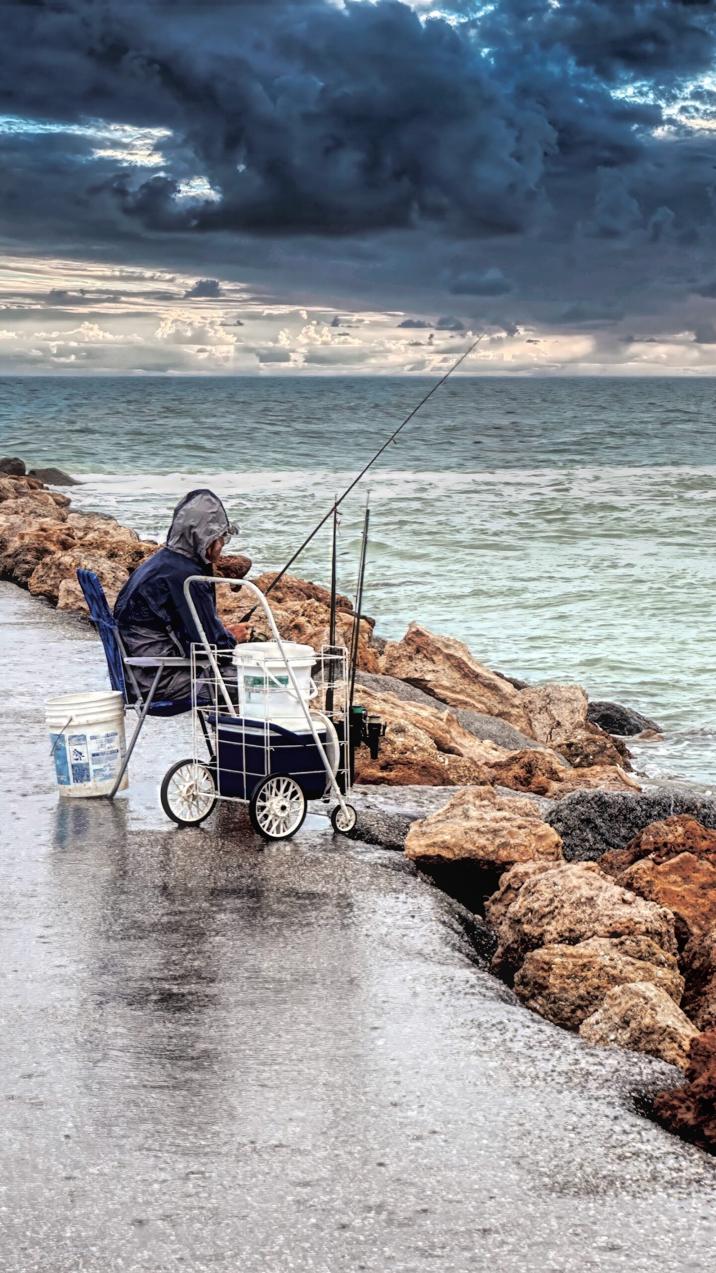 lone fisherman endures the rain at the Venice Jetties
